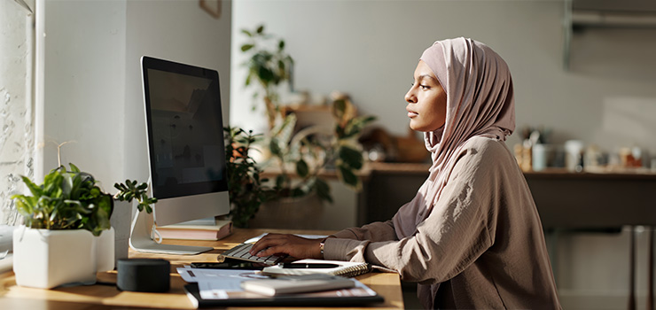 Young woman in a hijab working at a desktop computer