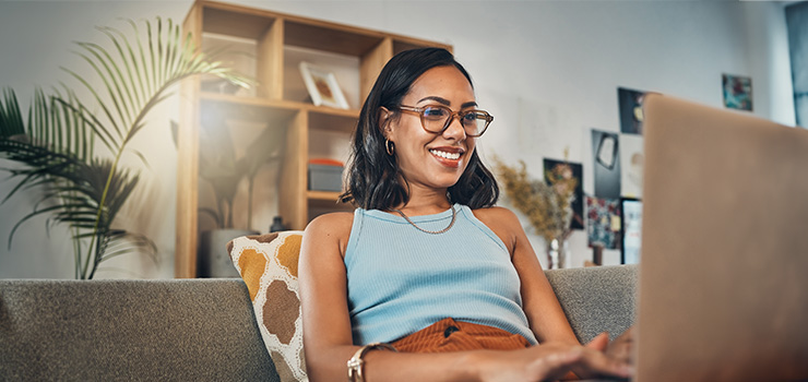 A smiling woman sat on a couch using a laptop