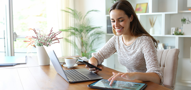 A smiling woman using a laptop and a tablet device