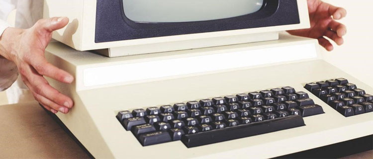 Very old desktop computer with built-in screen and keyboard placed on a desk by a person wearing a white coat