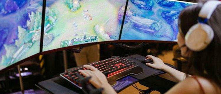 Woman playing PC game on triple monitor desktop setup using mouse and keyboard wearing headphones